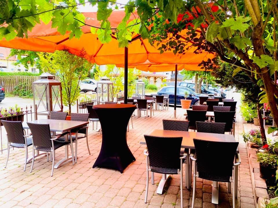 Ruhiger Biergarten unter Weinlaub und orangefarbenen Sonnenschirmen